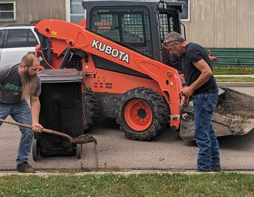 Open Door Capital district manager helping shovel dirt in front of a backhoe alongside the maintenance team, demonstrating hands-on support on-site.